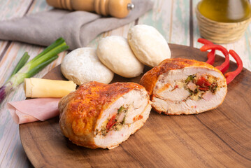 chicken roll stuffed with vegetables and ham and cheese with homemade bread on a round wooden plate with decorating ingredients