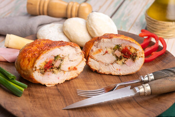 chicken roll stuffed with vegetables and ham and cheese with homemade bread on a round wooden plate with decorating ingredients
