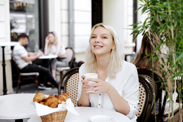 Stylish young woman drinking coffee on a restaurant terrace, feeling happy on a summer day
