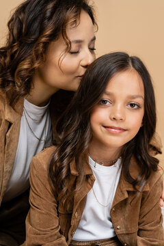 happy woman with closed eyes kissing hair of trendy daughter smiling at camera isolated on beige