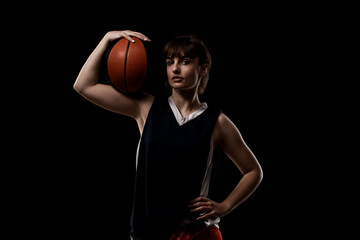 Female basketball player. Beautiful girl holding ball. Side lit half silhouette studio portrait...