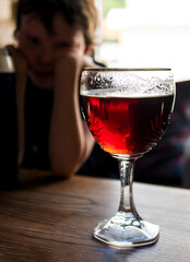 Beer glass and a sad child on the background. Parental problem drinking. Underage drinking
