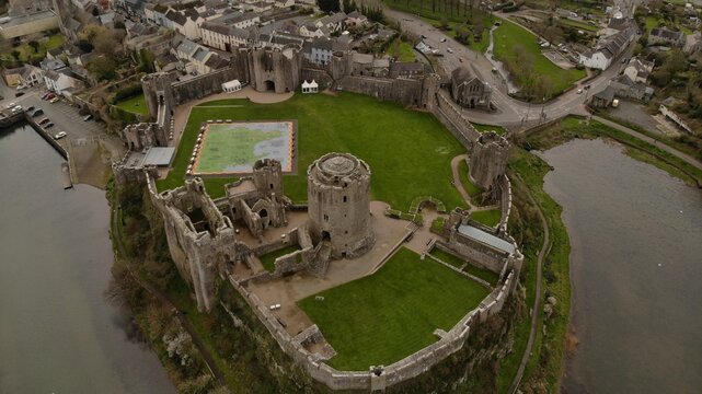 High angle of the Pembroke castle on a green hill top surrounded by buildings with water below