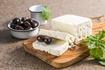 Feta cheese with olives and basil on a bamboo chopping board. The most famous Greek cheese.