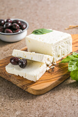 Feta cheese with olives and basil on a bamboo chopping board. The most famous Greek cheese.