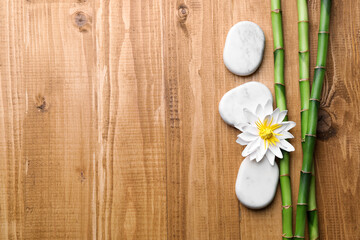 Fototapeta na wymiar Spa stones, flower and bamboo stems on wooden table, flat lay. Space for text