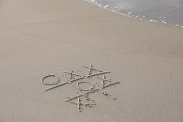 Tic tac toe game drawn on sand near sea, space for text