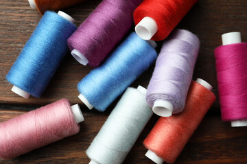 Different colorful sewing threads on wooden table, flat lay