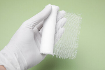 Doctor holding white bandage on light green background, closeup