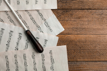 Conductor's baton and sheet music on wooden table, flat lay. Space for text
