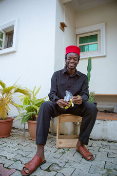 an igbo man eating groundnut and bananas outside his apartment
