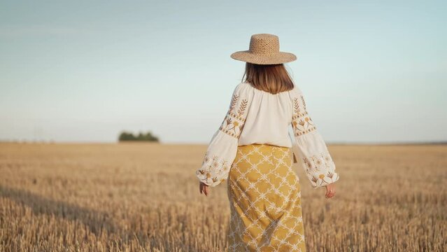 Attractive lady in embroidery vyshyvanka blouse and straw hat. Ukraine, independence, freedom, patriot symbol, stylish girl Unrecognizable ethnic woman walking in wheat field after harvesting. 
