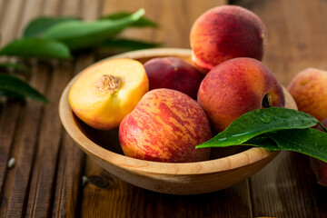 Peaches with leaves in a wooden bowl with peach in halves on top. Flat lay composition with ripe juicy peaches. Harvest of peaches for food or juice. Top view fresh organic fruit, vegan food.