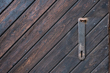Wooden door with a metal piece for attaching a padlock. Textured background, brown color. Copy Space