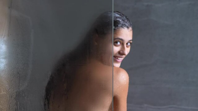 Beautiful young woman taking shower and looking over shoulder