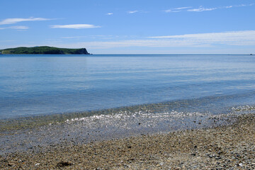 Sandy seashore with clear, transparent water with sun glare