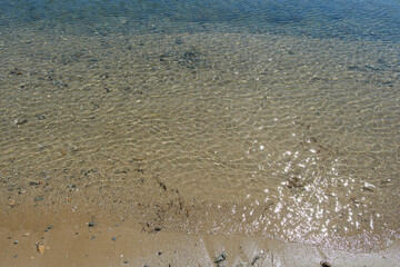 Sandy seashore with clear, transparent water with sun glare