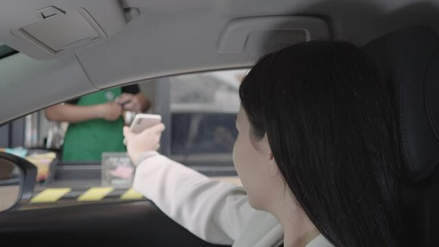 Beautiful woman is paying food or drinks with electronic wallet via smartphone scanning QR code by driving through or drive thru. Contactless payment.