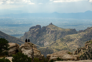 Two young women sitting on some rocks overlooking the Santa Catalina Mountains