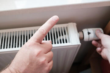 Forefinger makes a cautionary gesture and reminds of economy, against the background of a radiator. 