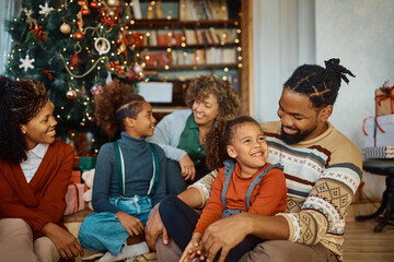 Happy black father and daughter talk while celebrating Christmas with their family at home.