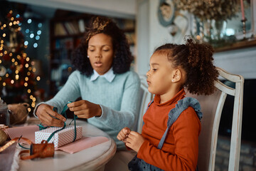 Small black girl decorating Christmas gift box with her mother at home.