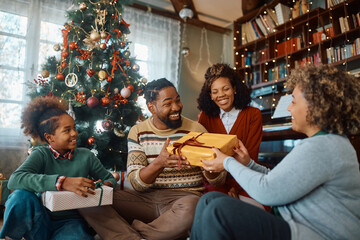 Fototapeta premium Happy black man receives Christmas present from his family at home.