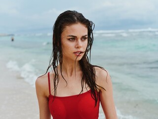 Fototapeta premium Beautiful woman on the beach by the sea in a red swimsuit