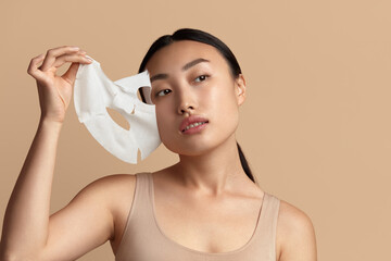 Woman Face Mask. Portrait Of Asian Girl Removing Cosmetic White Textile Mask from Facial Skin....