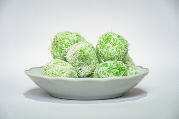 A traditional Indonesian snack called klepon, made from green glutinous rice and inside there is brown sugar, small round shape with grated coconut topping, served in a small bowl on a white backgroud