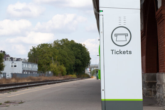 A ticket machine at a railway station is seen with no people on the platform. The "Tickets" machine is white and green. 