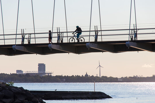 A cyclist crosses a bridge on a clear morning, in the far landscape a modern building and wind turbine can be seen. 