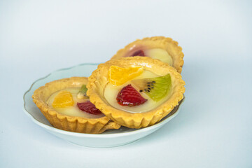 A small plate of a typical Indonesian snack called Pie Susu topped with slices of orange, strawberry and kiwi, served on a white background