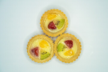 A small plate of a typical Indonesian snack called Pie Susu topped with slices of orange, strawberry and kiwi, served on a white background