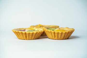 A small plate of a typical Indonesian snack called Pie Susu topped with slices of orange, strawberry and kiwi, served on a white background
