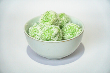 A traditional Indonesian snack called klepon, made from green glutinous rice and inside there is brown sugar, small round shape with grated coconut topping, served in a small bowl on a white backgroud