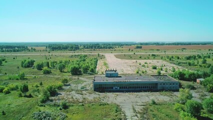 Aerial of a small abandoned airport in a valley with green trees and fields on a bright sunny day. Panoramic shot