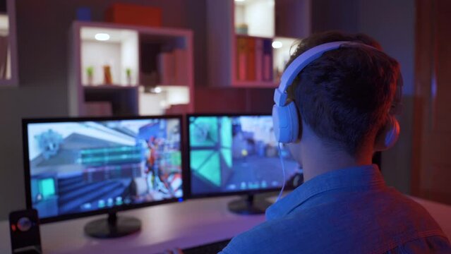 Professional Gamer Playing First Person Shooter Online Video Game on Powerful PC.
Young boy playing a game sitting in front of a computer, wearing headphones.
