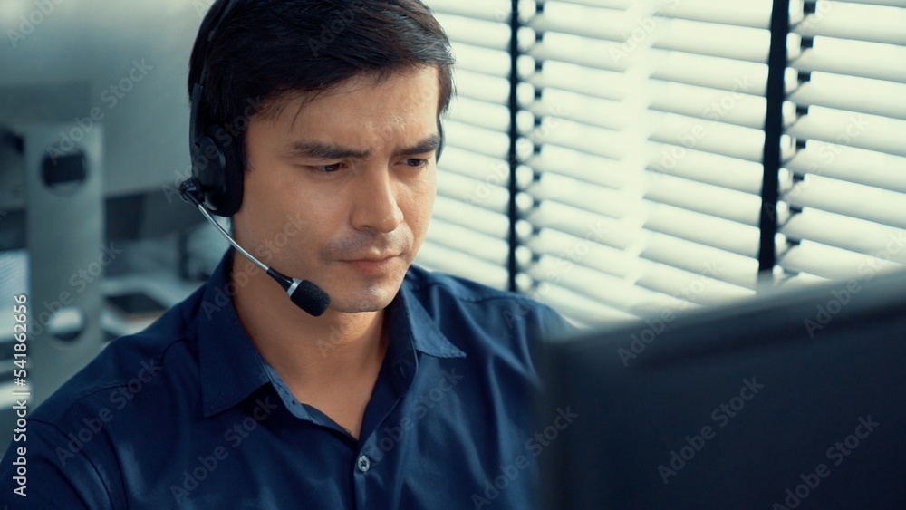 Aufkleber young competent asian male call center agent working at his computer while simultaneously speaking w