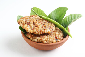 A crisp fried India snack called Sabudana Vada made from tapioca seeds, roasted peanuts, boiled potato and herbs served in a terracotta bowl placed on a white background 