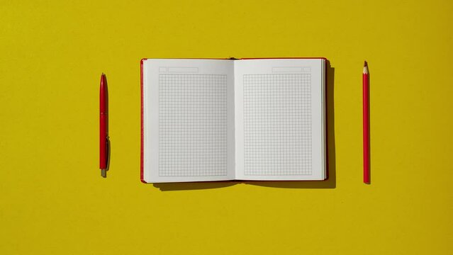 Red notebook diary on yellow office table at home workspace for notes and reminders.