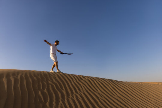 Handsome Man playing tennis on a barkhan in the desert