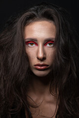 Fashion and make-up concept. Studio portrait of beautiful woman with red eye shadows, long and dark dreadlocks hair looking at camera with seductive look. Studio shot in black background