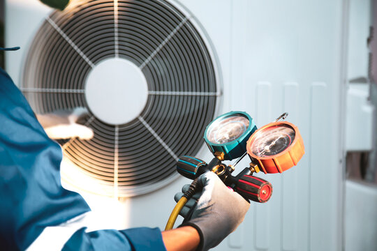 Mechanic air conditioner technician using manifold gauge checking refrigerant for filling home air conditioning and air duct cleaning and maintenance outdoor compressor unit.