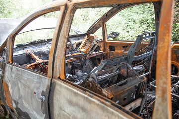 Fototapeta na wymiar Car after a fire. Burnt rusty car after fire or accident. Car after the fire, crime of vandalism, riots. Arson car. Accident on the road due to speeding. Explosion.