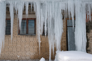 Obraz na płótnie Canvas Big icicles on the roof of a townhouse on a snowy winter day among thaw. Cleaning the roofing from snow and icicles.