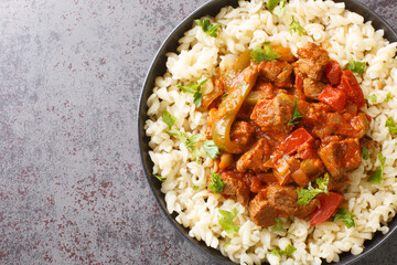 Porkolt is a Hungarian stew with boneless meat, paprika and some vegetables served with Egg Noodles Nokedli closeup on the plate on the table. Horizontal top view from above