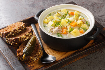 Zupa Ogorkowa Cucumber soup is a traditional Polish and Lithuanian soup made from sour, salted cucumbers and root vegetables closeup on the pot on the wooden tray. Horizontal