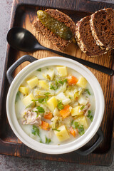 Dill pickle soup zupa ogorkowa is one of the most popular traditional soups in Poland closeup on the pot on the wooden tray. Vertical top view from above