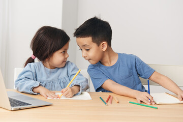 children draw with colored pencils sitting at the table and talking to each other